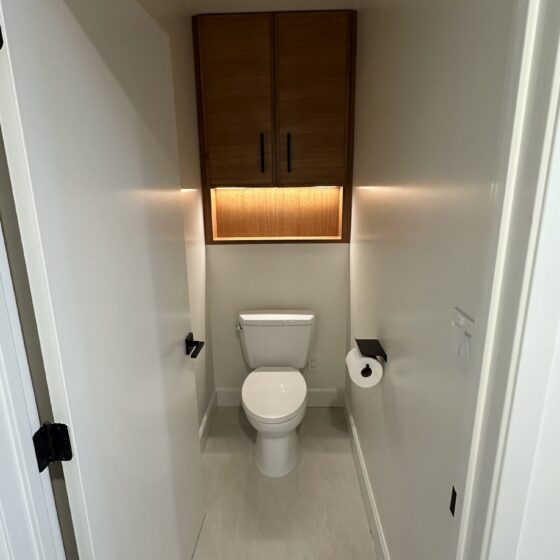 Separate water closet with a wood wall cabinet and black hardware in a Birdland master bathroom
