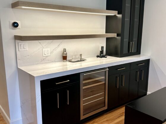 Dry bar with black cabinets, glass-front upper cabinet, wine fridge and floating shelves in a Birdland home