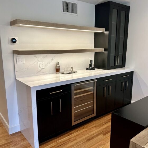 Dry bar with black cabinets, glass-front upper cabinet, wine fridge and floating shelves in a Birdland home