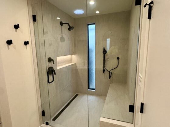 Walk-in glass shower with bench, niche and black fixtures in a Birdland master bathroom
