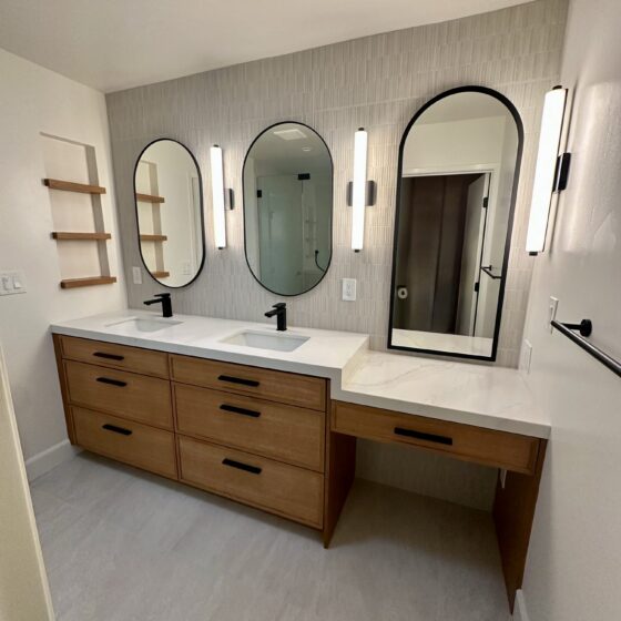 Master bathroom double vanity with wood drawers, arched mirrors and vertical sconces in a Birdland home